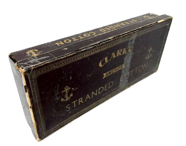 May include: A vintage box of Clark's Anchor Stranded Cotton. The box is brown with gold lettering and an anchor logo. The text on the box reads "Clark's Anchor Stranded Cotton Fast Color."