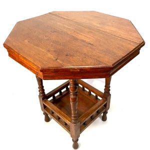 May include: A wooden, octagonal side table with a dark brown finish. The table features a decorative lower shelf and turned legs. The tabletop is approximately 61 cm in diameter.