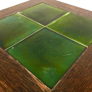 May include: A square table with a wooden frame and a tiled top. The tiles are a glossy green, arranged in a diamond pattern. The wooden frame has a dark brown finish, showing the wood grain. The table is likely around 60 cm in length.