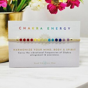 May include: A gold chain bracelet with seven colorful beads representing the seven chakras. The bracelet is on a white card with the text "CHAKRA ENERGY" and "HARMONIZE YOUR MIND, BODY & SPIRIT Carry the vibrational frequencies of Chakra alignment & awareness. Good Vibrations Shop."