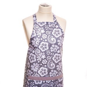 Könnte beinhalten: Eine graue Schürze mit einem weißen floralen Spitzenmuster und einer braunen Tasche.