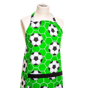 Könnte beinhalten: Grüne Schürze mit Fußballmuster. Die Schürze hat eine schwarze Tasche und verstellbare Träger.
