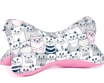 Puede incluir: Una almohada de viaje rosa y gris con un patrón de gatos de dibujos animados. La almohada tiene forma de hueso y tiene una textura suave y mullida.