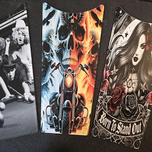 May include: Three motorcycle gas tank covers with different designs. The first shows a group of people playing pool. The second shows a skull with flames and a motorcycle. The third shows a woman with a rose and the text "Born to Stand Out".
