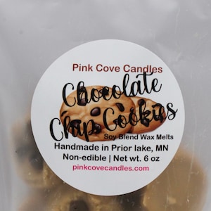 May include: A white label with the text "Pink Cove Candles Chocolate Chip Cookies Soy Blend Wax Melts Handmade in Prior lake, MN Non-edible | Net wt. 6 oz pinkcovecandles.com" and a graphic of two chocolate chip cookies.