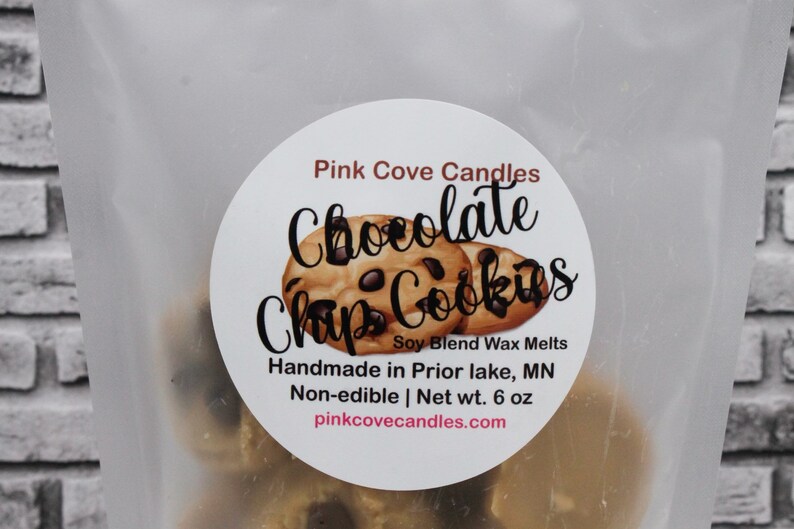 May include: A white label with the text "Pink Cove Candles Chocolate Chip Cookies Soy Blend Wax Melts Handmade in Prior lake, MN Non-edible | Net wt. 6 oz pinkcovecandles.com" and a graphic of two chocolate chip cookies.