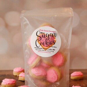 K&ouml;nnte beinhalten: Eine transparente Plastikt&uuml;te gef&uuml;llt mit rosa und wei&szlig;en Mini-Zuckerkeks-Duftwachs-Schmelzen. Die T&uuml;te hat ein Etikett mit der Aufschrift "Pink Cove Candles Mini Sugar Cookies Para Soy Wax Melts Handmade in Prior Lake, MN Non-edible | Net wt. 4 oz (113.4 g) pinkcovecandles.com".