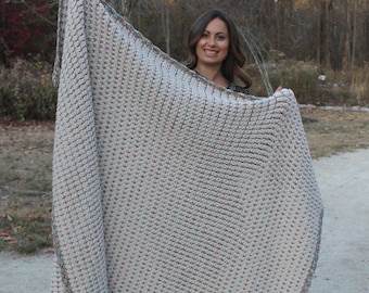 May include: A large, crocheted throw blanket in a beige color with a subtle multi-colored fleck pattern. The blanket has a crocheted border in a darker beige color.