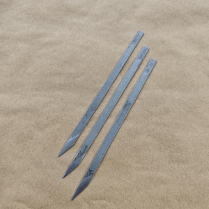 Puede incluir: Tres pinchos de metal plateado con extremos puntiagudos. Los pinchos están etiquetados con "10" y "12" en negro.