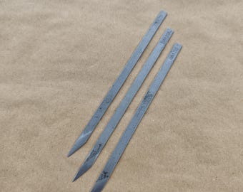 May include: Three silver metal skewers with pointed ends. The skewers are labeled "10" and "12" in black.
