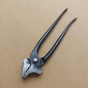 Könnte beinhalten: Ein schwarzes Metallwerkzeug mit langen, gebogenen Griffen und einem strukturierten Kopf. Das Werkzeug hat einen Drehpunkt in der Mitte und ist zum Greifen oder Schneiden bestimmt. Der Kopf trägt den Text "FABERGS ESKILSTUNA SWEDEN" und die Nummer "502".