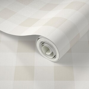 Puede incluir: Un rollo de papel tapiz con un patr&oacute;n de cuadros grandes en tonos suaves de beige y blanco. El material tiene un acabado de superficie sutil y finamente texturizado, y el papel est&aacute; parcialmente desenrollado para mostrar el dise&ntilde;o.