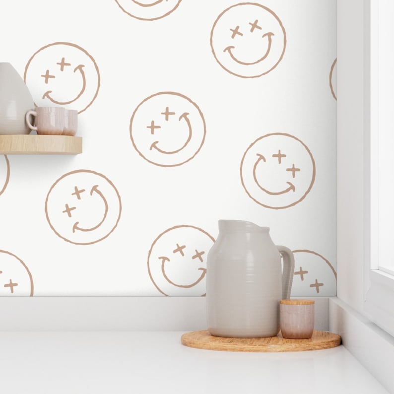 May include: White wall with a brown smiley face pattern. A white pitcher and a small white jar are on a wooden coaster on a white countertop.