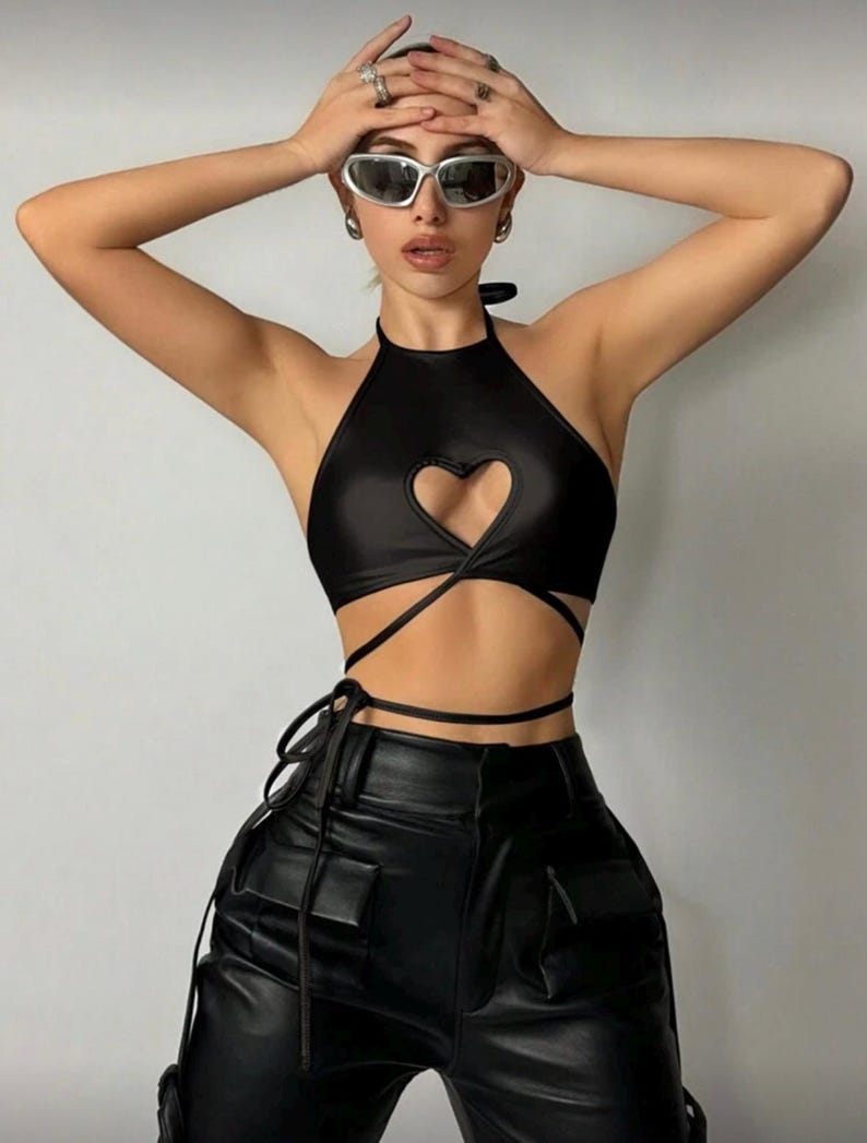 May include: Black halter top with a heart-shaped cutout and wrap-around ties. The top is paired with black leather pants. The outfit is a stylish ensemble.