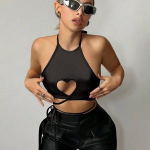 May include: A black halter top with a heart-shaped cutout and tie closure. The top is paired with black leather pants. The model is wearing silver sunglasses and rings.