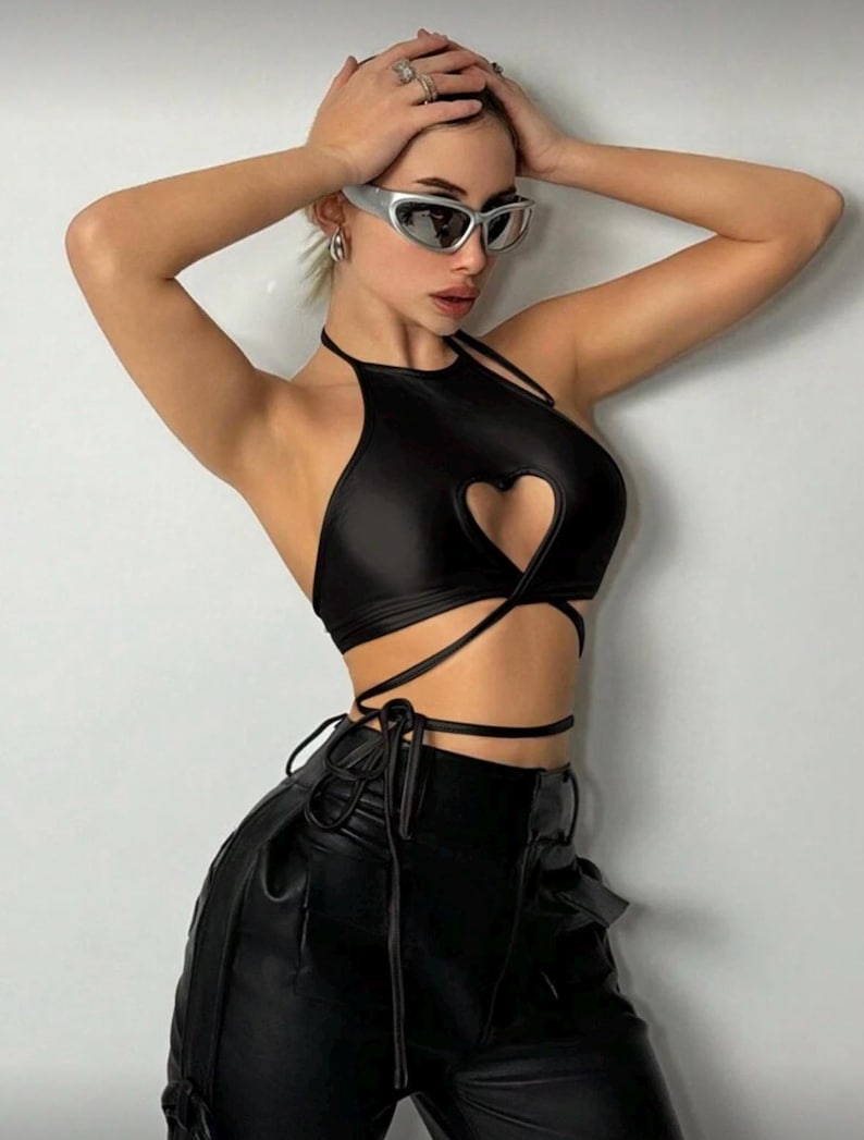 May include: Black halter top with a heart-shaped cutout and wrap-around ties. The top is paired with black leather pants. Silver-framed sunglasses are worn.