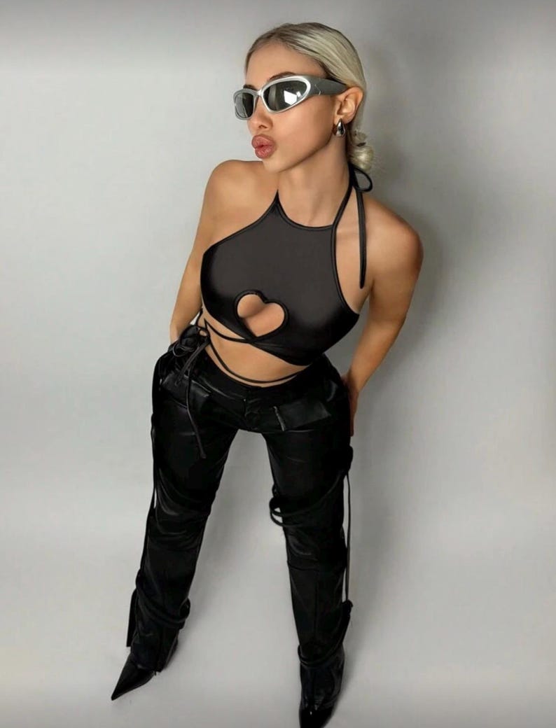 May include: Black halter top with a heart-shaped cutout and matching black pants. The pants have decorative straps and pointed-toe boots. The model is wearing silver-framed sunglasses.