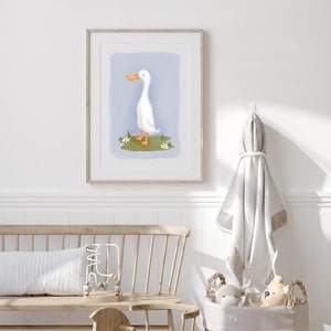 May include: A framed illustration of a white duck with an orange beak standing on a patch of green grass with white flowers. The background is a light blue color.