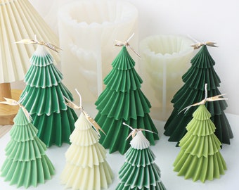 May include: A set of seven green and white layered Christmas tree candles. The candles are arranged on a white surface. The candles are made in a variety of sizes.