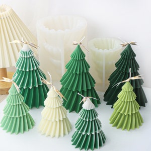 May include: A set of seven green and white layered Christmas tree candles. The candles are arranged on a white surface. The candles are made in a variety of sizes.