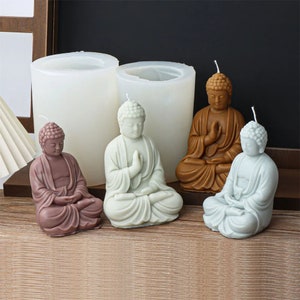 May include: Four Buddha candle molds, two white silicone molds and two finished candles, one brown and one light gray. The candles are sitting on a wooden surface.
