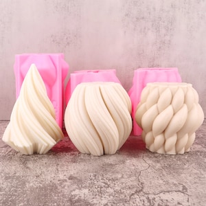 Puede incluir: La imagen muestra tres moldes de velas texturizados de color blanquecino en varias formas, incluyendo un cono y dos formas redondeadas. Detrás hay tres moldes de silicona rosas. Los moldes están diseñados para la elaboración de velas o artículos decorativos similares.