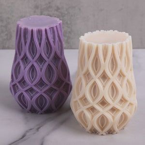 May include: Two decorative candles, one purple and one cream, with an intricate geometric pattern. The candles are shaped like a vase and have a smooth, polished finish.