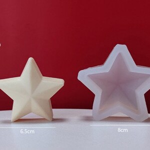 May include: Two white silicone star-shaped molds for making candles or soap. The larger mold measures 8 cm wide and 7.4 cm tall. The smaller mold measures 6.5 cm wide and 6.2 cm tall.