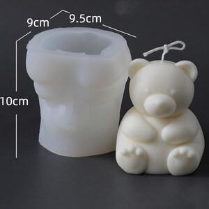 May include: A white bear-shaped candle next to a white silicone mold. The candle has a wick and is sitting. The mold is 10 cm tall, 9 cm wide, and 9.5 cm across the top. The candle and mold are on a dark background.
