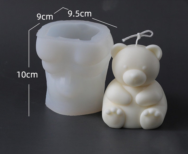 May include: A white bear-shaped candle next to a white silicone mold. The candle has a wick and is sitting. The mold is 10 cm tall, 9 cm wide, and 9.5 cm across the top. The candle and mold are on a dark background.