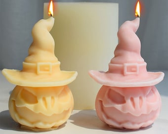 May include: Two Halloween-themed candles shaped like jack-o'-lanterns wearing witch hats. The candle on the left is yellow and the candle on the right is pink.