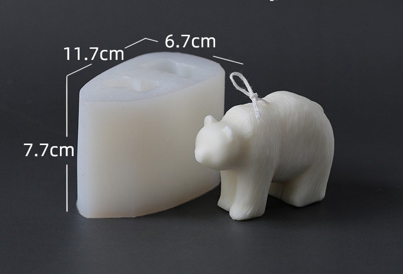 May include: A white bear-shaped candle and its silicone mould. The candle has a wick and is 6.7 cm wide, 7.7 cm tall, and 11.7 cm long. The mould is the same shape and size as the candle. The background is a dark grey.