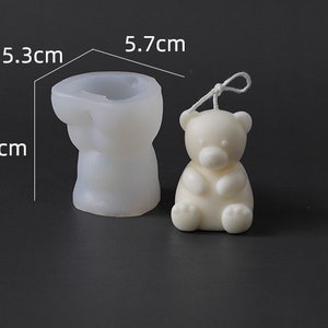 May include: A white bear-shaped candle and a silicone mold. The candle is 5.7 cm tall. The mold is 7 cm tall and 5.3 cm wide. The candle has a string attached. The items are on a dark surface.