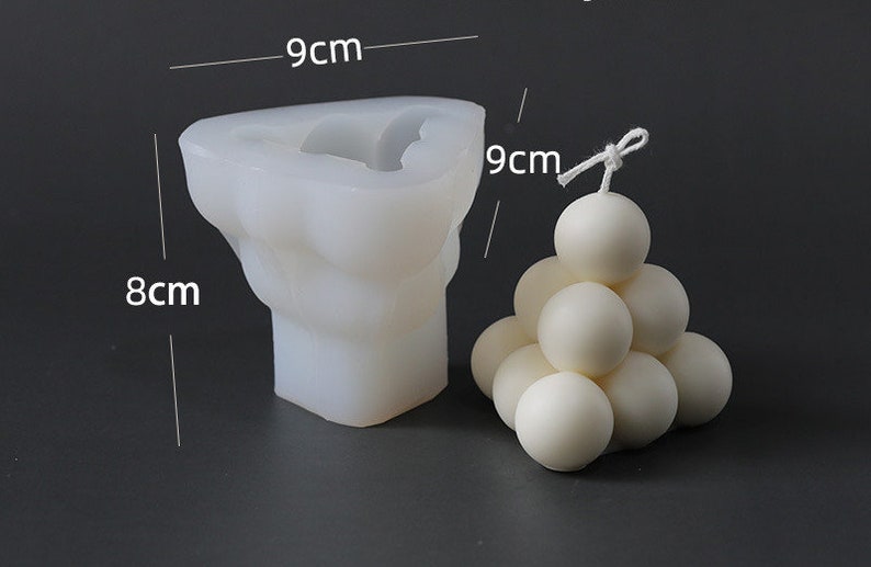 May include: A white silicone candle mould, 8cm x 9cm, next to a finished white sphere candle. The mould is in the shape of a torso. The sphere candle is made of multiple spheres stacked in a pyramid shape. Candle making supplies.