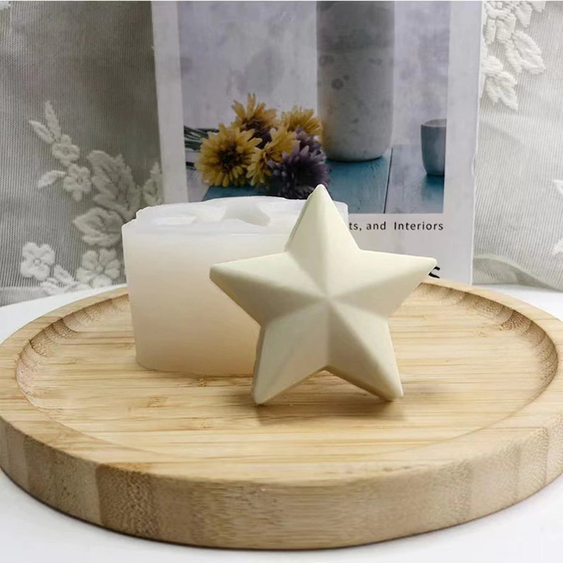May include: A white star-shaped candle on a wooden tray. The candle is made in a silicone mold, which is also visible in the image.