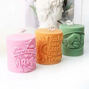 Può includere: Tre candele a pilastro con diversi design. La candela rosa dice "World's Best Mama" con un design di uccello e fiori. La candela arancione dice "Teachers Plant Seeds That Grow Forever" con un design di girasole. La candela verde ha un design a pugno in rilievo.