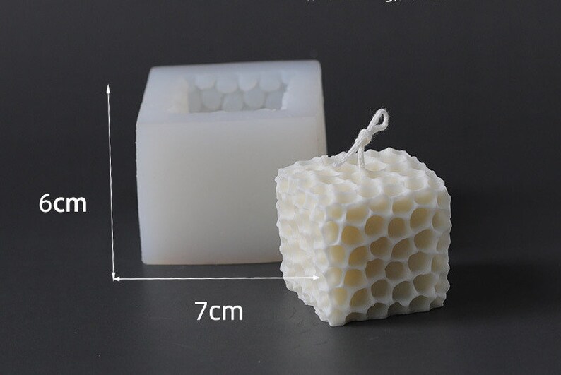 May include: A white, cube-shaped candle with a honeycomb pattern, next to a silicone mold. The candle measures approximately 7 cm wide and 6 cm tall. A white wick is visible at the top of the candle. The mold is 7 cm wide and 6 cm tall.