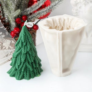 Puede incluir: Un molde de silicona blanco para hacer una vela de árbol de Navidad. El molde tiene forma de árbol de Navidad y tiene un acabado liso y brillante. El molde se muestra junto a una vela de árbol de Navidad verde que se ha hecho utilizando el molde.