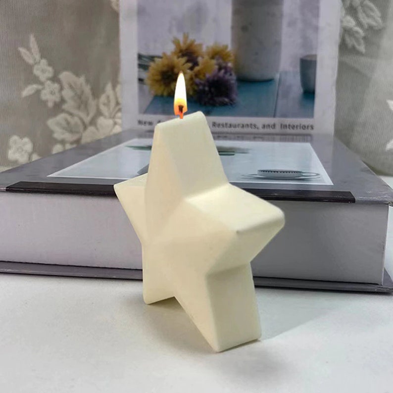 May include: A white star-shaped candle with a lit wick. The candle is sitting on a white surface.