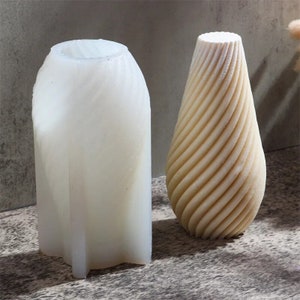 May include: Two white ceramic vases with a swirl design. The vase on the left is taller and has a more cylindrical shape. The vase on the right is shorter and has a more rounded shape.