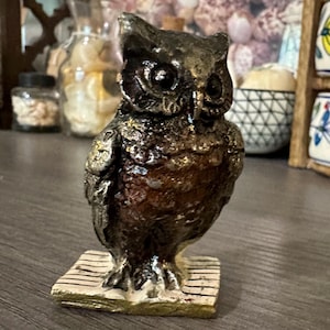 May include: A small, detailed owl figurine with a brown and gold finish. The owl is perched on a base with a striped pattern.