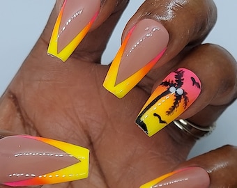 May include: Coffin-shaped press-on nails featuring a nude base with vibrant yellow and neon pink V-shaped French tips. One nail showcases a detailed sunset scene with a black palm tree silhouette against a yellow, orange, and pink gradient background.