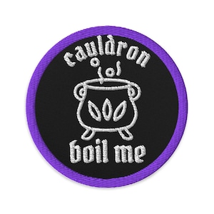 Puede incluir: Un parche bordado circular con fondo negro y borde morado. El diseño presenta un caldero blanco bordado con vapor saliendo de él, rodeado por el texto blanco "cauldron" arriba y "boil me" debajo de la imagen.