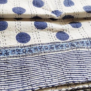 Puede incluir: Textil plegado con fondo blanco y grandes lunares azules. El diseño incluye un borde floral azul y un patrón de rayas en la parte inferior. La tela parece estar cosida.