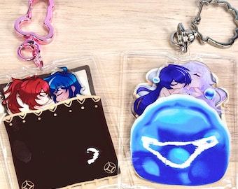 May include: Two clear acrylic keychains with colorful anime characters. One keychain features two characters sleeping in a bed, the other features two characters in a blue bubble.