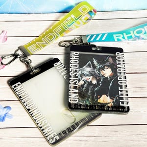 May include: Two lanyards and ID badge holders with the text "ENDFIELD INDUSTRIES" and "RHODES ISLAND". One ID holder features an anime-style illustration. The lanyards are yellow and blue with silver clasps.