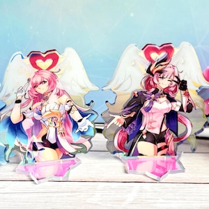 May include: Two anime-style character acrylic stands. The character on the left has pink hair, a white dress, and wings. The character on the right has pink and purple hair, a black and white dress, and wings. Both characters are standing on clear acrylic bases.