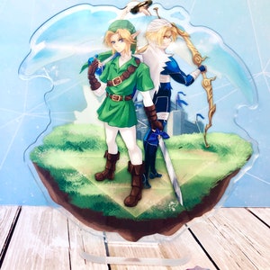 May include: A clear acrylic keychain featuring two anime characters, one in green and one in blue, standing on a green and brown island. The characters are holding swords and a bow and arrow. The background is a blue sky with white clouds.