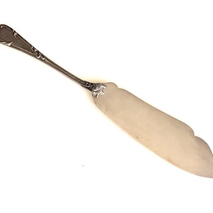 May include: A silver butter knife with an ornate handle and a scalloped edge.