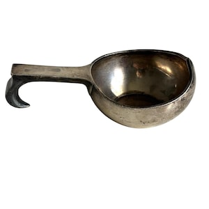 Op de afbeelding: Een zilverkleurige ijsschep met een gebogen handvat. De schep heeft een afgeronde komvorm en een handvat dat aan het uiteinde buigt. Het metaal heeft een licht aangeslagen uiterlijk.